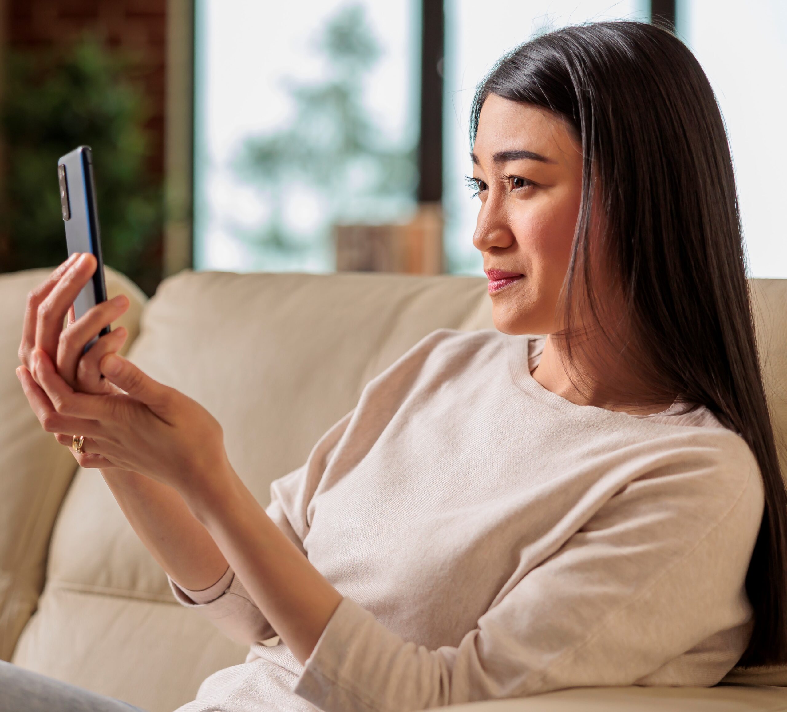 Casual looking happy Asian woman using smartphone at home