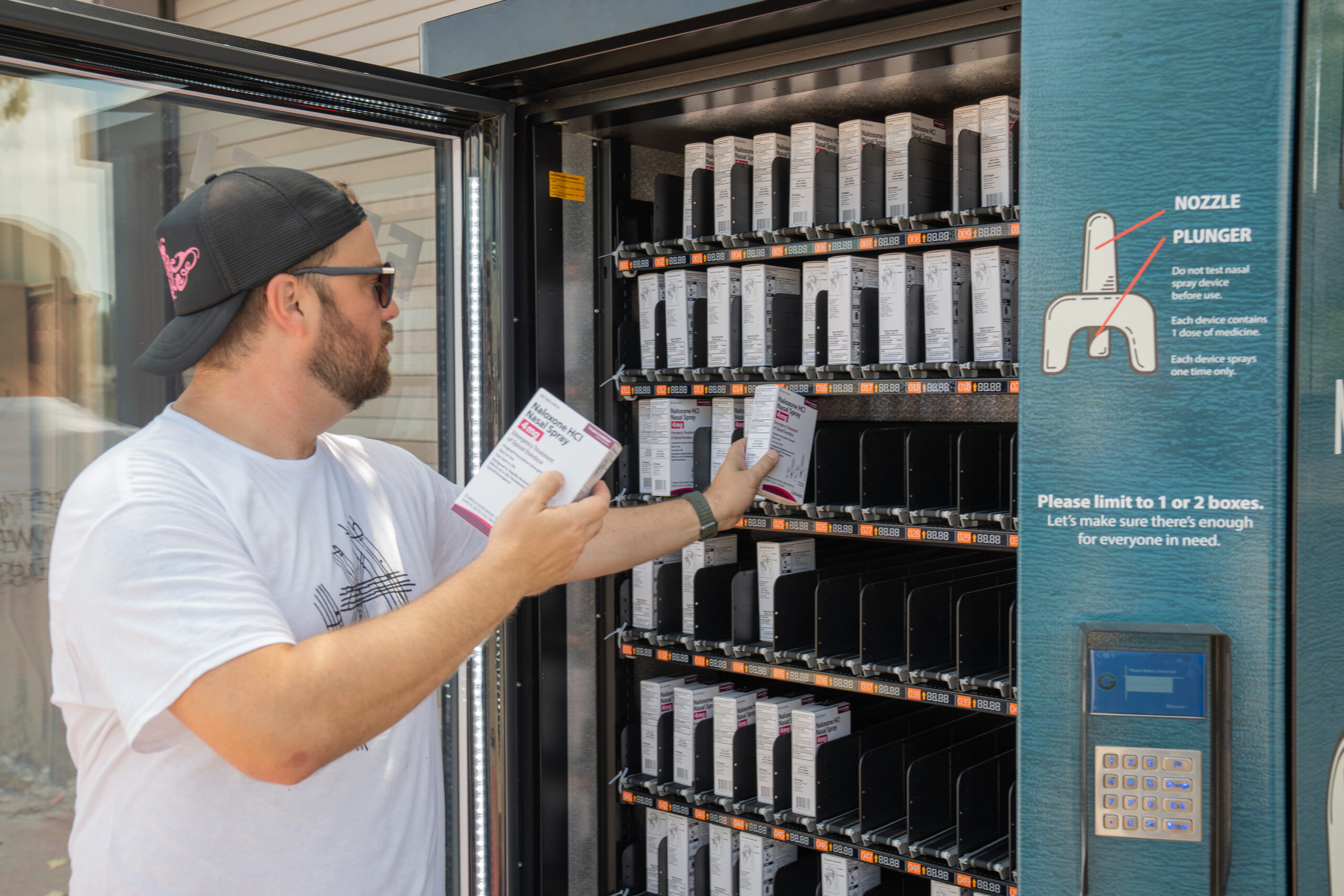 A man is placing boxes of naloxone into a naloxone vending machine