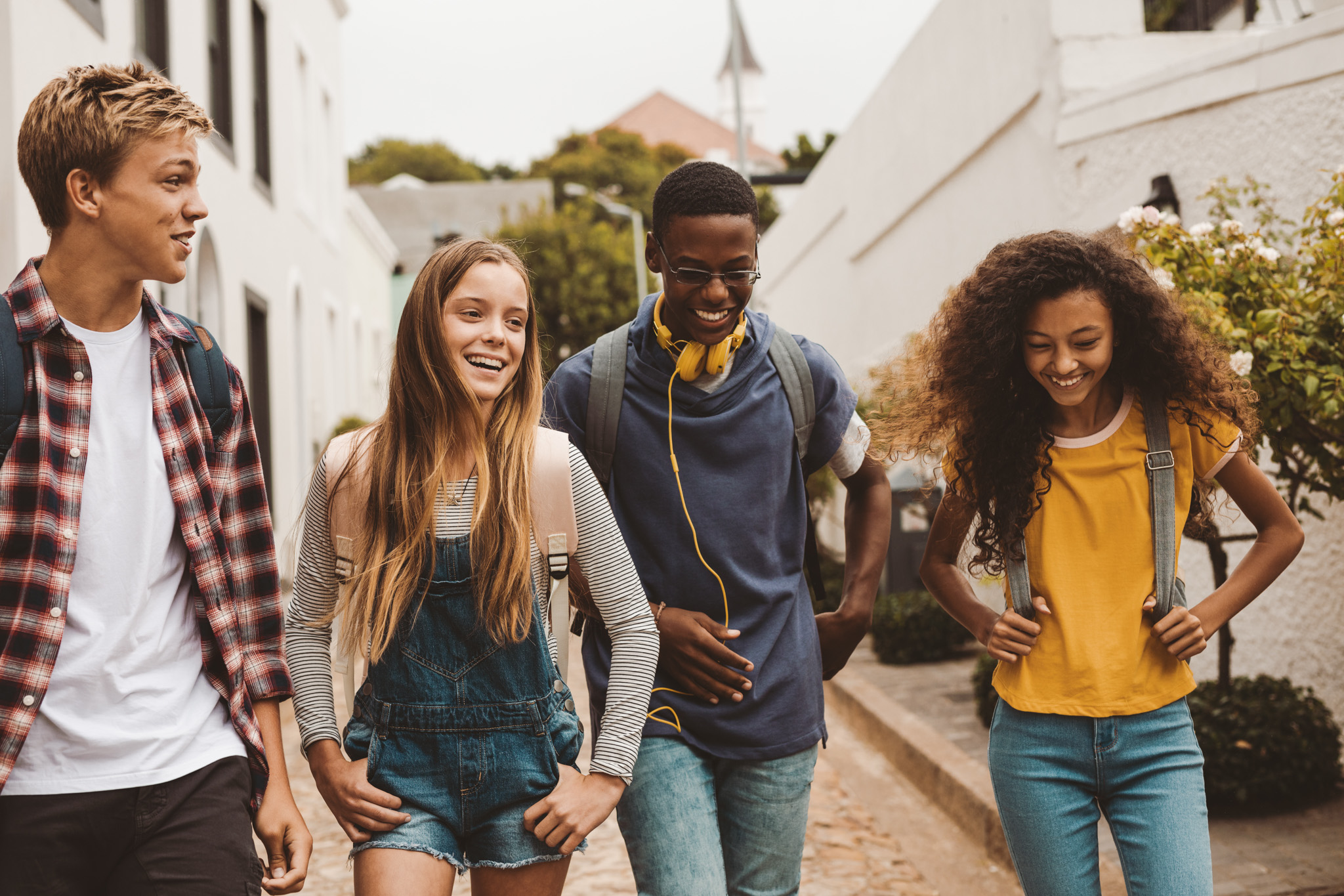 Smiling teenage friends wearing backpacks walking outdoors and talking.